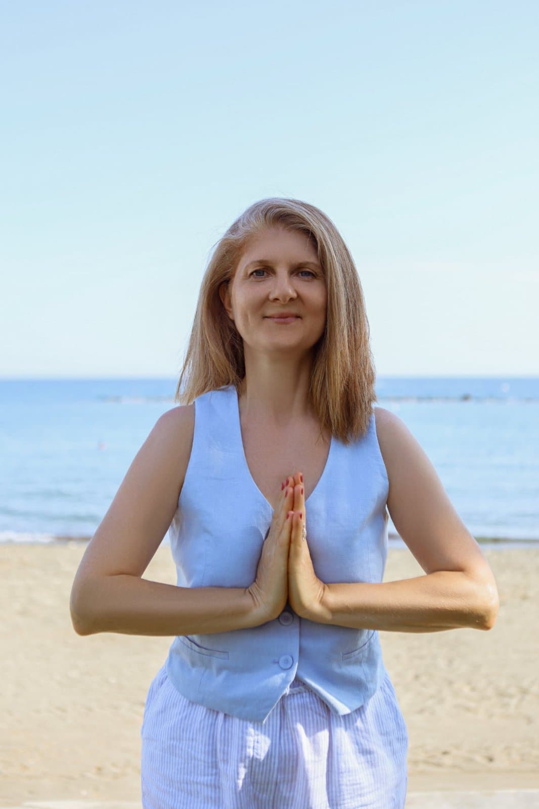 Dona in white by the sea, hands folded in namaste