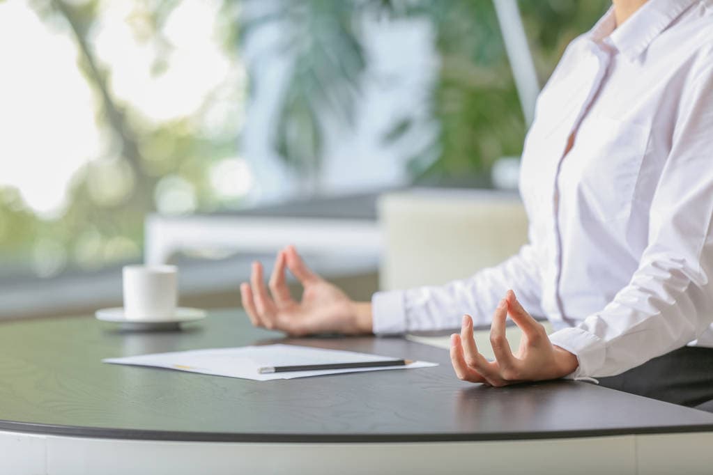 A businesswoman meditating cross-legged at her office desk
